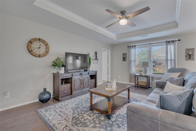 living room with ceiling fan, a raised ceiling, wood-type flooring, and ornamental molding