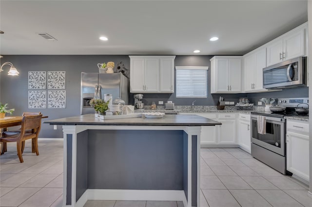 kitchen featuring appliances with stainless steel finishes, a kitchen island, hanging light fixtures, white cabinetry, and light tile patterned floors