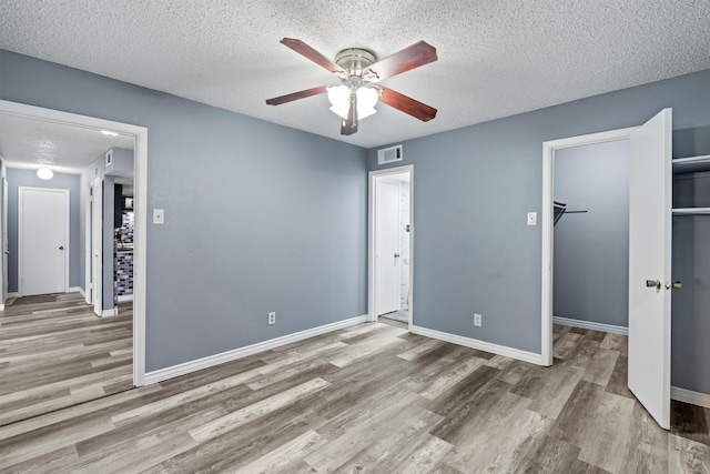 unfurnished bedroom featuring hardwood / wood-style flooring, ceiling fan, a textured ceiling, and a walk in closet