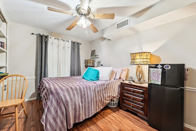 bedroom featuring ceiling fan, hardwood / wood-style floors, and black refrigerator