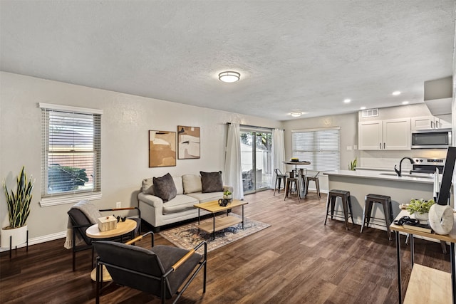 living room featuring sink, a healthy amount of sunlight, dark hardwood / wood-style flooring, and a textured ceiling