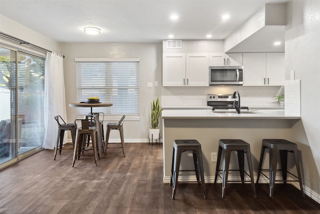 kitchen featuring appliances with stainless steel finishes, backsplash, white cabinets, dark hardwood / wood-style floors, and a breakfast bar area