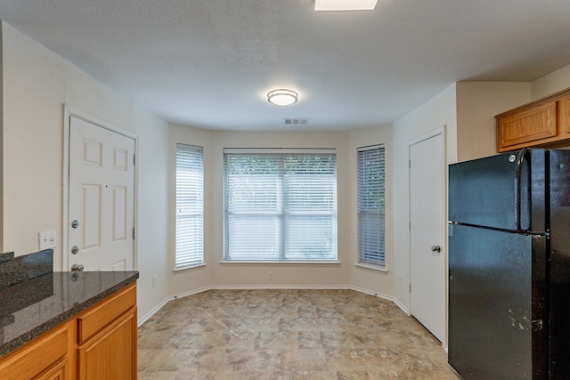 kitchen with a textured ceiling, black refrigerator, and dark stone counters