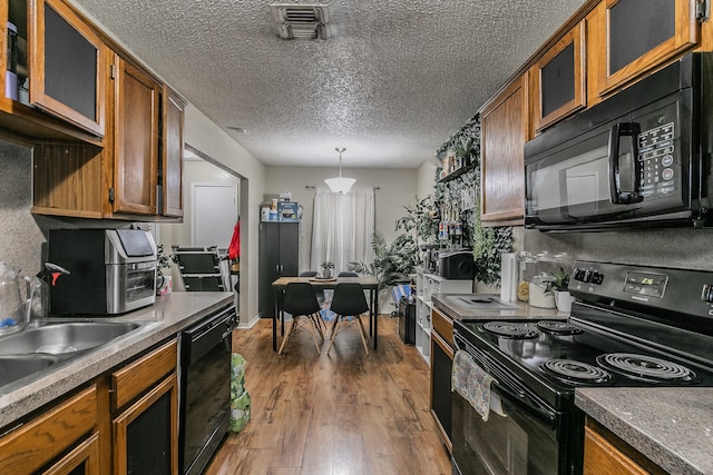 kitchen with dark wood-type flooring, hanging light fixtures, a textured ceiling, black appliances, and sink