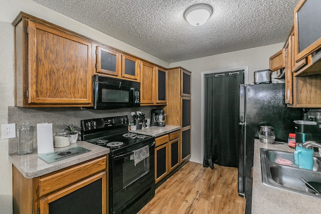 kitchen with light hardwood / wood-style floors, a textured ceiling, sink, and black appliances