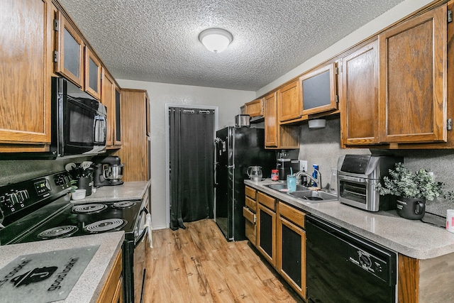 kitchen featuring a textured ceiling, light hardwood / wood-style floors, black appliances, and sink