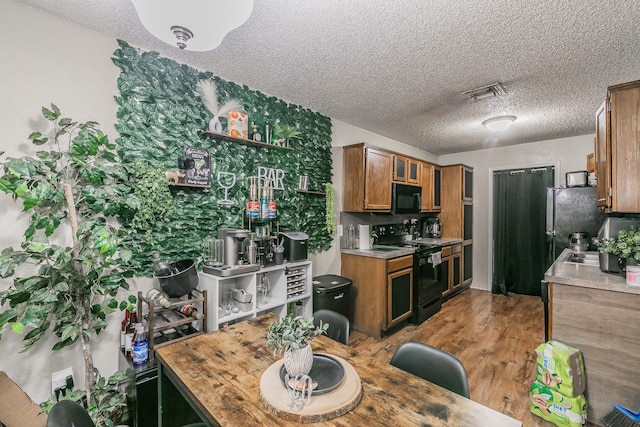 kitchen with black appliances, hardwood / wood-style floors, and a textured ceiling