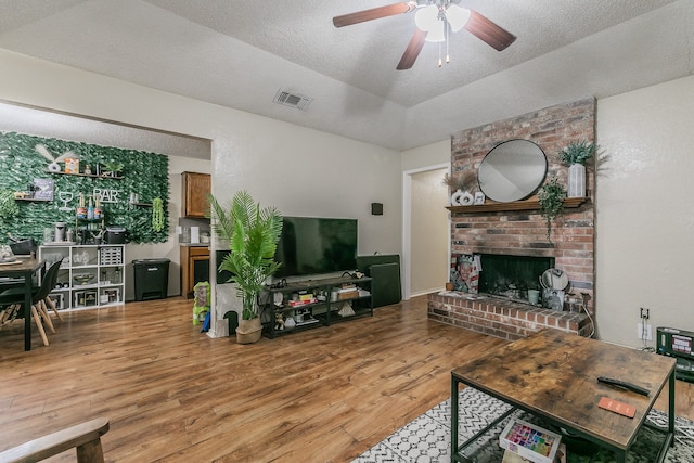 living room with hardwood / wood-style floors, a fireplace, a textured ceiling, and ceiling fan