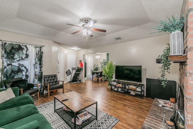 living room with a textured ceiling, hardwood / wood-style flooring, ceiling fan, and a raised ceiling