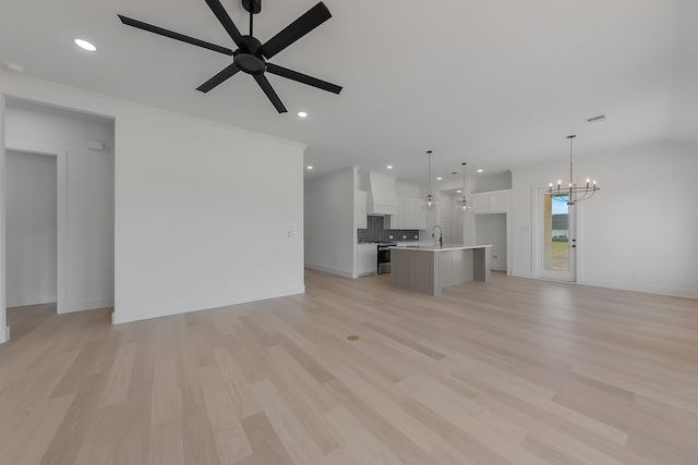 unfurnished living room with sink, ceiling fan with notable chandelier, and light wood-type flooring