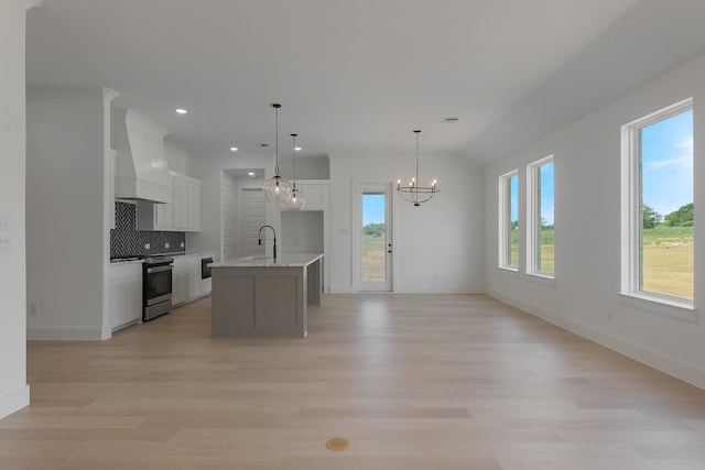 kitchen with stainless steel range, custom exhaust hood, a kitchen island with sink, and plenty of natural light