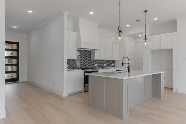 kitchen featuring sink, stainless steel range, light hardwood / wood-style flooring, premium range hood, and a center island with sink