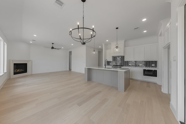 kitchen featuring a center island with sink, pendant lighting, white cabinetry, light hardwood / wood-style floors, and tasteful backsplash