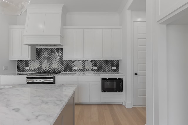 kitchen featuring light wood-type flooring, stainless steel range with gas stovetop, white cabinetry, custom exhaust hood, and black microwave