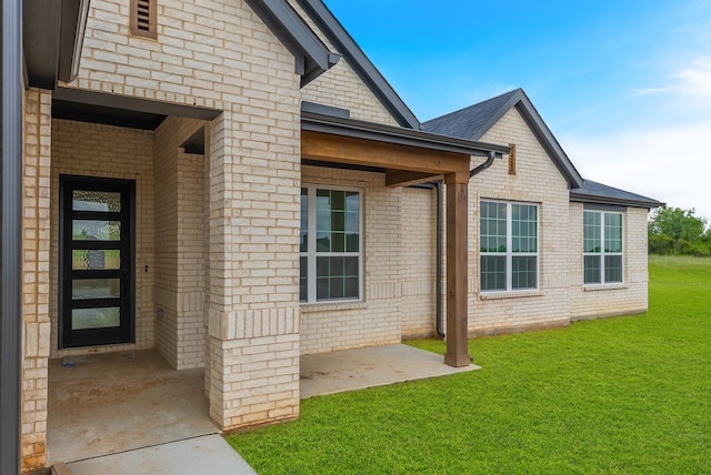 view of exterior entry featuring a yard and a patio