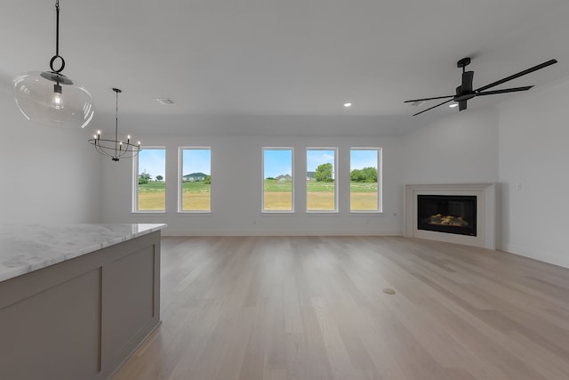 unfurnished living room featuring light hardwood / wood-style floors, a healthy amount of sunlight, and ceiling fan with notable chandelier