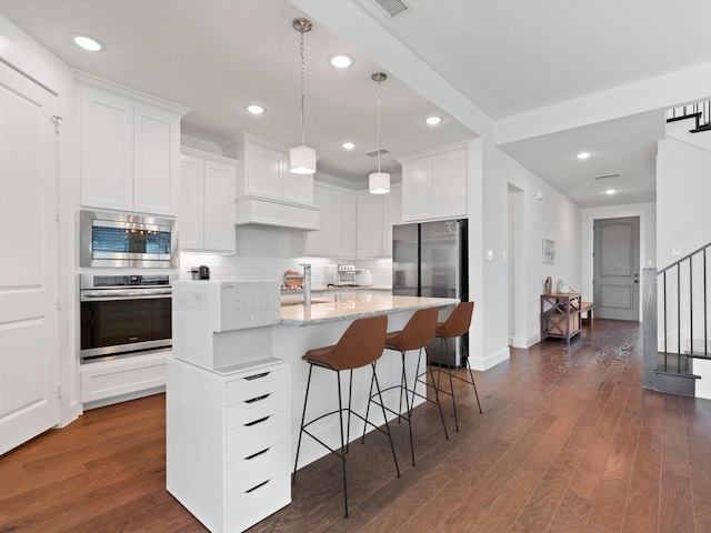 kitchen featuring white cabinetry, appliances with stainless steel finishes, a kitchen island with sink, and pendant lighting