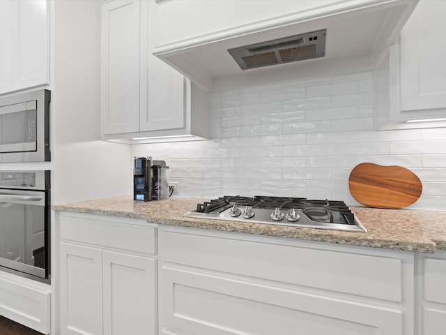 kitchen with tasteful backsplash, stainless steel appliances, light stone countertops, and white cabinets