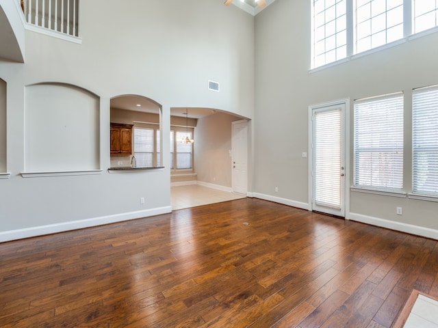 unfurnished living room with a towering ceiling, an inviting chandelier, and dark wood-type flooring