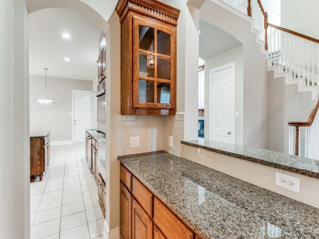 kitchen featuring tasteful backsplash, light tile patterned floors, stone counters, pendant lighting, and a notable chandelier