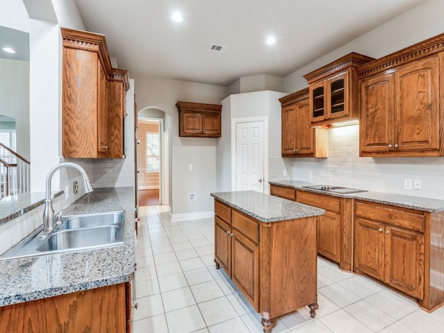 kitchen with electric cooktop, decorative backsplash, light stone counters, a kitchen island, and sink