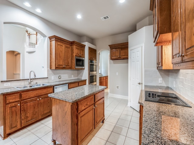 kitchen featuring appliances with stainless steel finishes, light tile patterned flooring, sink, a kitchen island, and light stone counters