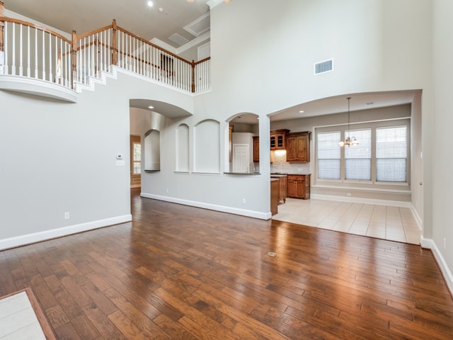 unfurnished living room featuring a towering ceiling, a notable chandelier, and wood-type flooring