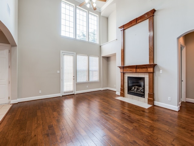 unfurnished living room featuring ceiling fan, wood-type flooring, a high ceiling, and a tile fireplace