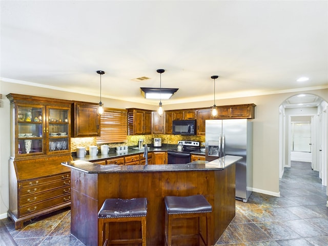 kitchen featuring a breakfast bar, pendant lighting, backsplash, stainless steel appliances, and a center island with sink