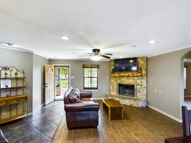 living room with crown molding, a stone fireplace, dark hardwood / wood-style flooring, and ceiling fan