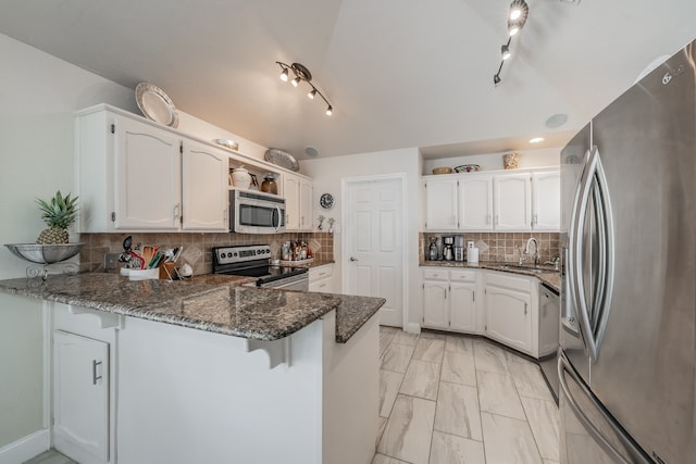 kitchen featuring kitchen peninsula, decorative backsplash, appliances with stainless steel finishes, white cabinetry, and dark stone counters