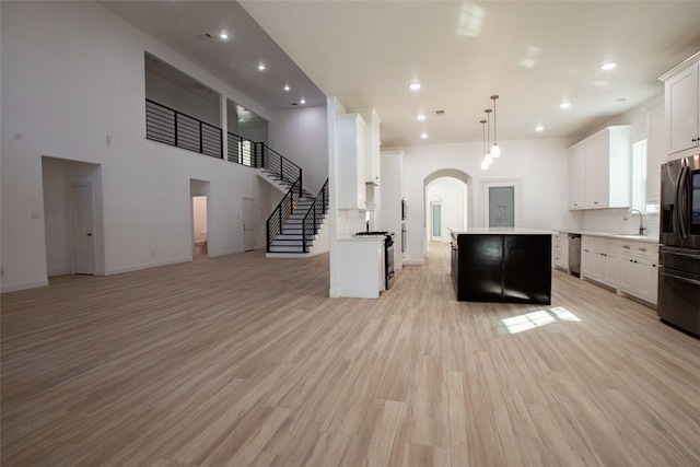 kitchen featuring white cabinets, hanging light fixtures, a kitchen island, appliances with stainless steel finishes, and light wood-type flooring