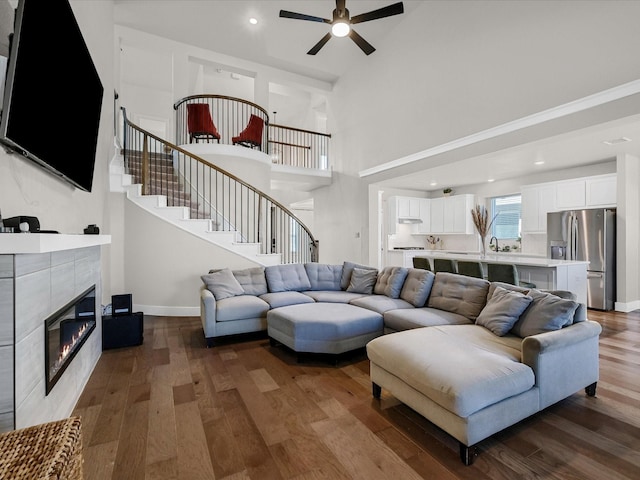 living area featuring baseboards, a tile fireplace, ceiling fan, wood finished floors, and stairs