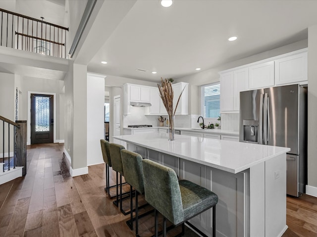 kitchen with white cabinetry, a breakfast bar area, a center island, stainless steel fridge with ice dispenser, and dark hardwood / wood-style flooring