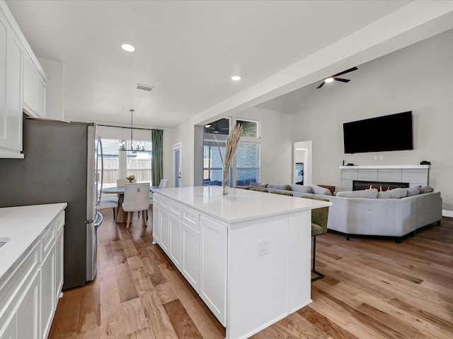 kitchen featuring white cabinetry, open floor plan, hanging light fixtures, freestanding refrigerator, and a center island with sink