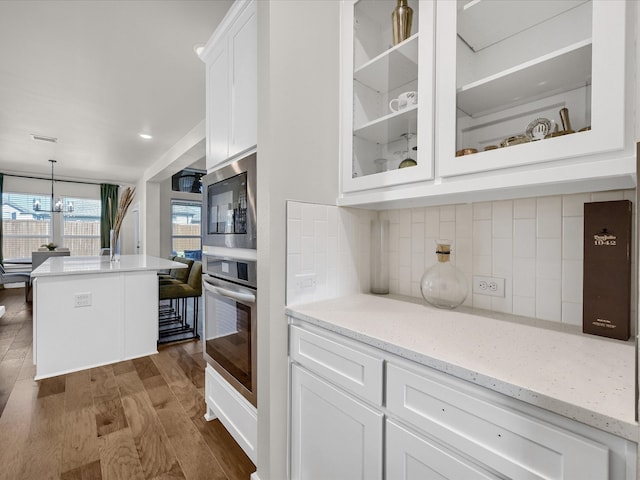 kitchen with white cabinetry, light stone counters, appliances with stainless steel finishes, decorative light fixtures, and dark hardwood / wood-style flooring