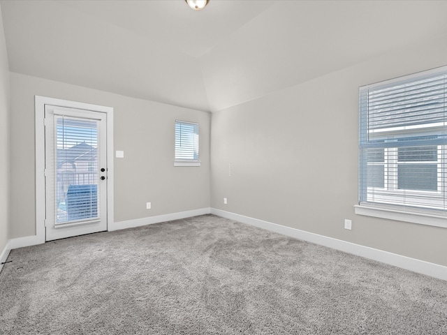 carpeted spare room featuring baseboards and vaulted ceiling