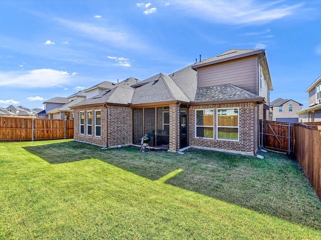 rear view of house featuring brick siding, a lawn, a shingled roof, and a fenced backyard