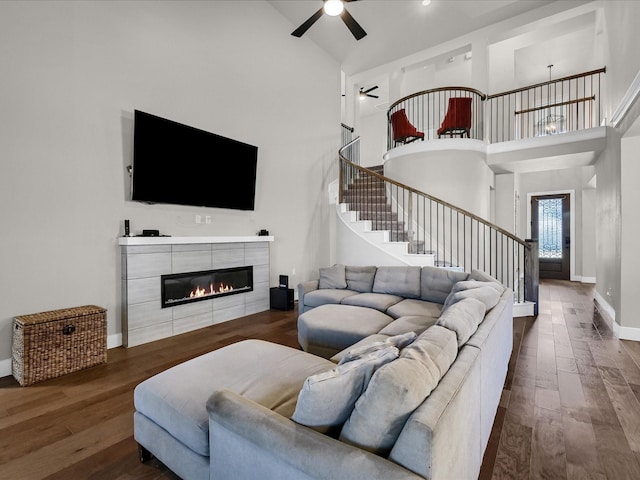 living room featuring a ceiling fan, wood finished floors, stairs, a fireplace, and high vaulted ceiling