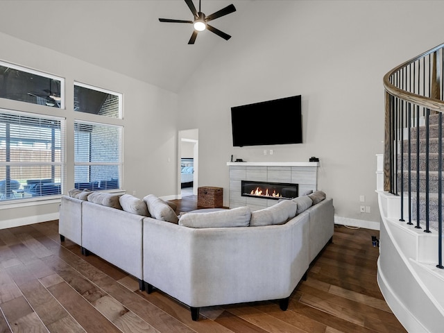 living room featuring dark wood-type flooring, ceiling fan, a tile fireplace, and high vaulted ceiling