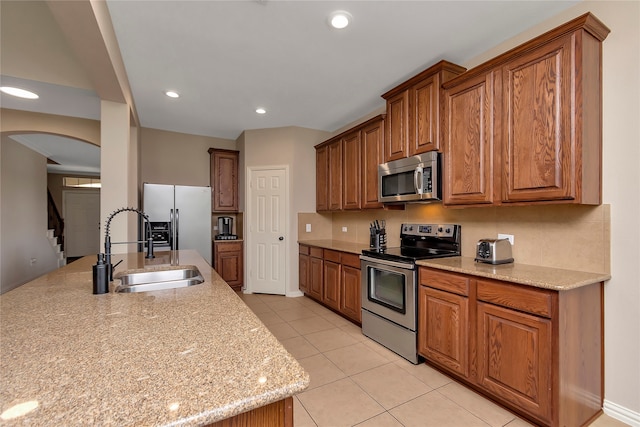 kitchen with light stone counters, light tile patterned flooring, appliances with stainless steel finishes, and sink