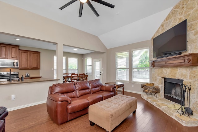 living room with a stone fireplace, ceiling fan, wood-type flooring, and vaulted ceiling