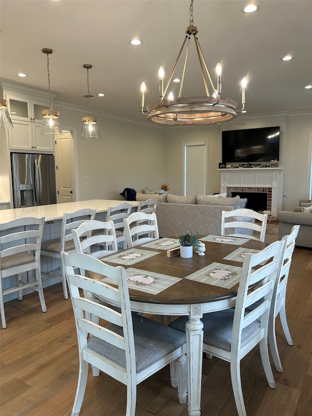 dining space featuring crown molding, a chandelier, dark hardwood / wood-style floors, and a brick fireplace