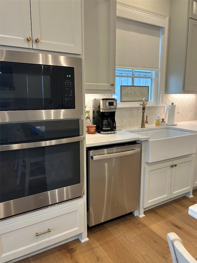 kitchen with backsplash, stainless steel appliances, sink, light hardwood / wood-style flooring, and white cabinets