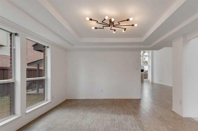 empty room featuring wood-type flooring, an inviting chandelier, and a tray ceiling