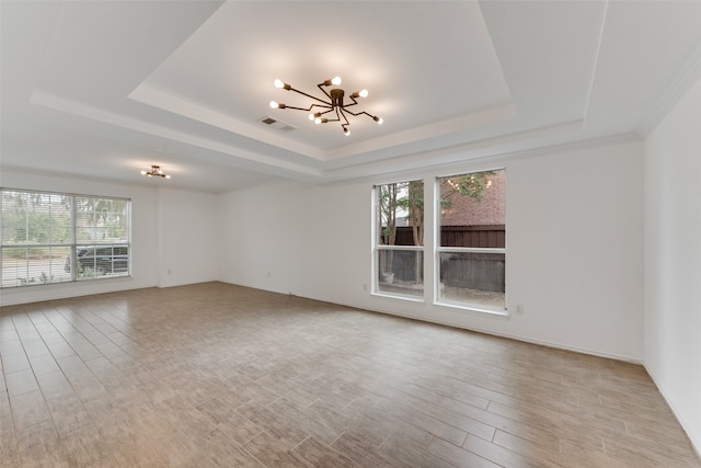 spare room featuring light wood-type flooring, a tray ceiling, and a notable chandelier