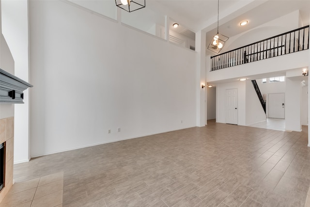 unfurnished living room featuring a towering ceiling, a tile fireplace, and light hardwood / wood-style floors