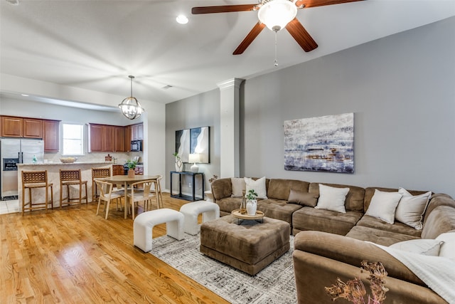 living room with ornate columns, ceiling fan with notable chandelier, and light wood-type flooring