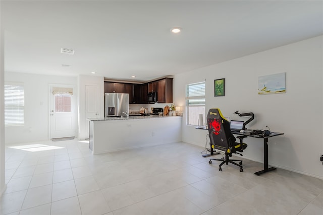 kitchen featuring light tile patterned floors, kitchen peninsula, dark brown cabinets, light stone countertops, and stainless steel fridge with ice dispenser