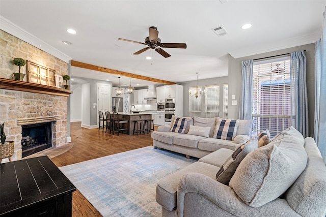 living room featuring a stone fireplace, ceiling fan with notable chandelier, dark hardwood / wood-style flooring, and ornamental molding